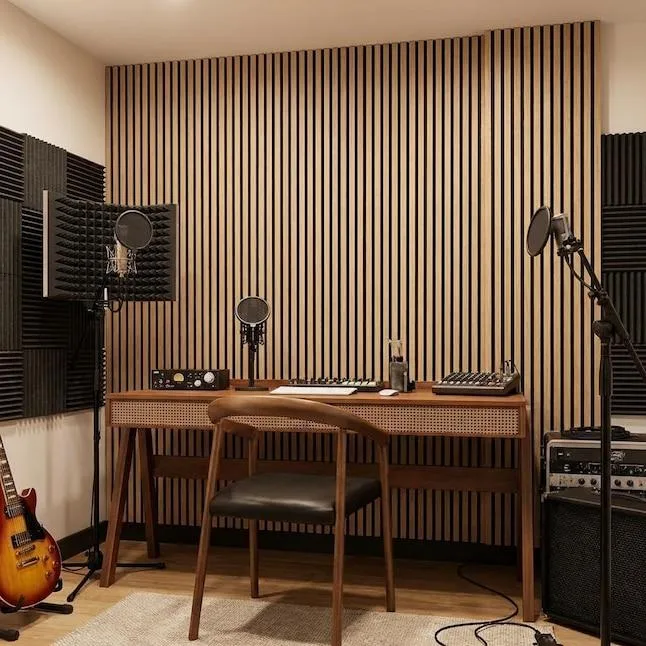 Puesto de grabación frente a una pared de listones verticales de madera, con dos micrófonos con filtro antipop, equipo en rack, una guitarra eléctrica y paneles de espuma en las paredes laterales.