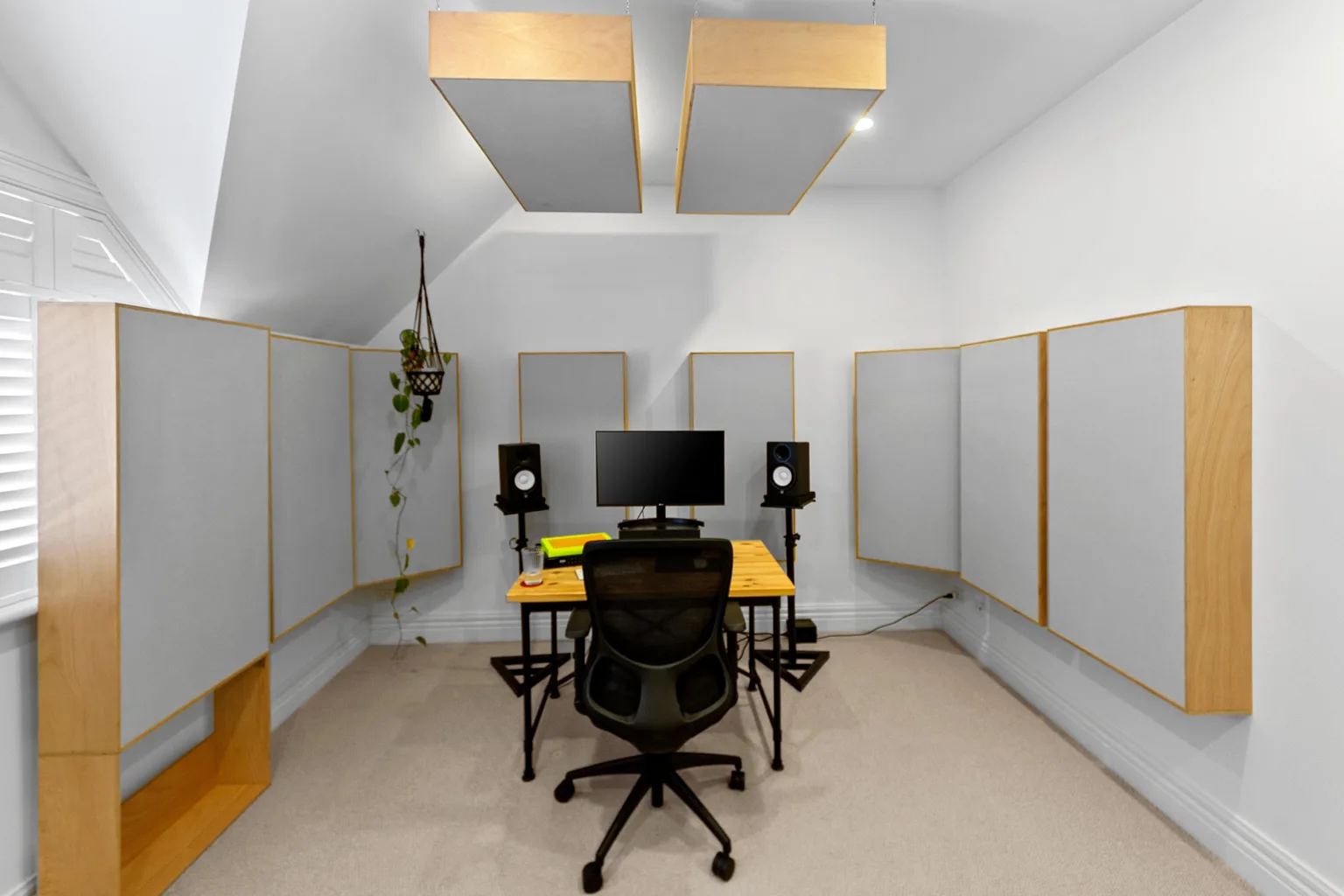 Sala con paneles enmarcados en madera en ambas paredes laterales y dos paneles suspendidos del techo, con un escritorio central, monitores sobre soportes y una silla de trabajo.